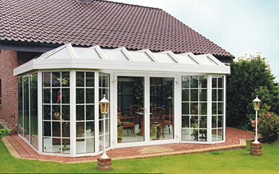 Wintergarten mit weißem Aluminiumrahmen, Glas-Satteldach und Rundelementen, Blick auf gepflegten Garten.