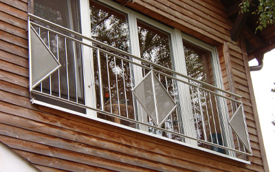 Edelstahlbalkongeländer mit dekorativen Metallelementen an Holzfassade eines Wohnhauses