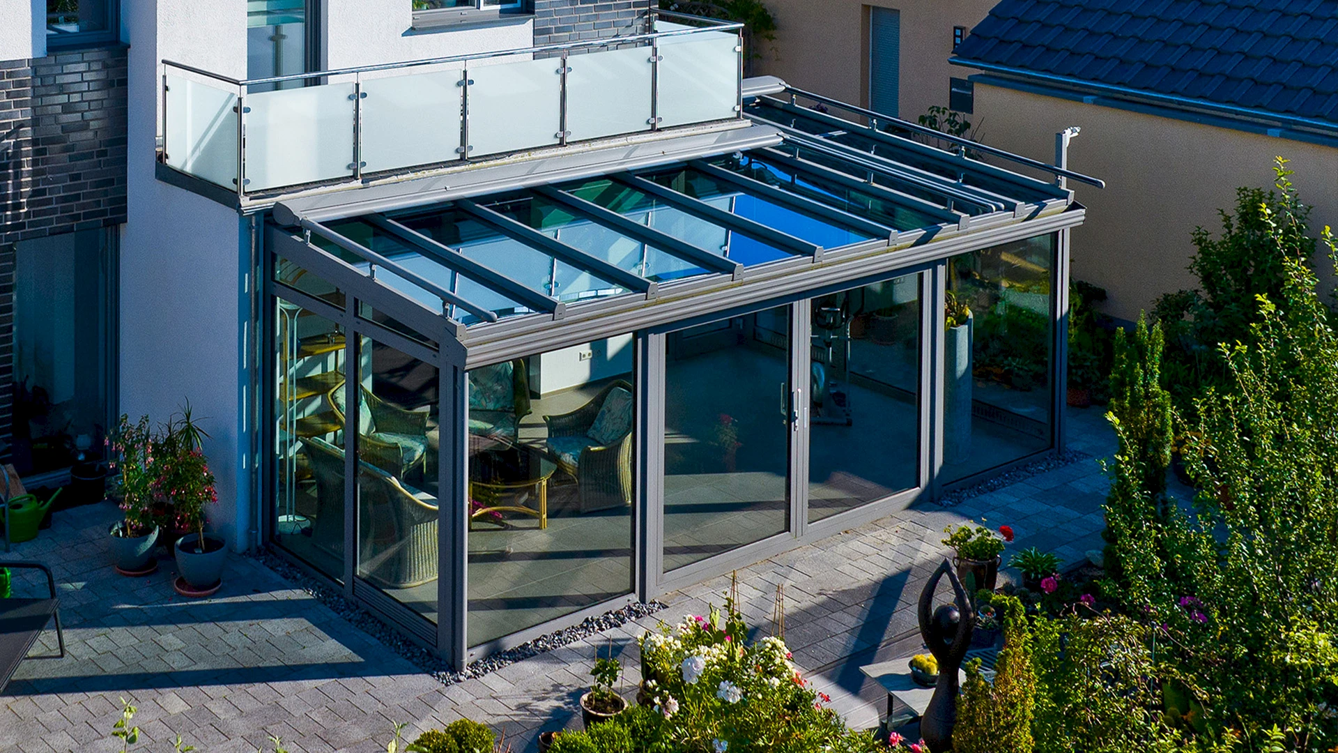 Moderner Wintergarten mit Pultdach und Glasdachkonstruktion, angebaut an ein Einfamilienhaus mit Terrasse und Garten