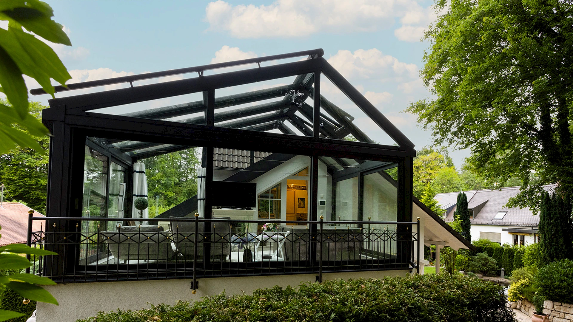 Moderner Wintergarten mit Satteldach aus schwarzem Aluminium und großflächiger Verglasung auf einer Terrasse mit Gartenumgebung