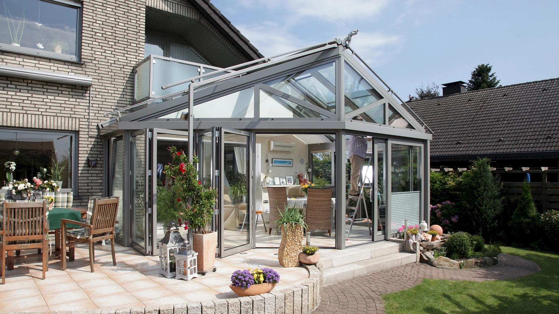 Heller Wintergarten mit Satteldach aus Aluminium und Glas, angebaut an ein Einfamilienhaus mit Terrasse und Garten