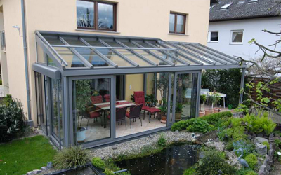 Heller Wintergarten mit Glasdach, Schiebeelementen und Blick in den Garten mit Teich