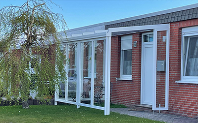 Terrassenüberdachung mit weißen Profilen und Glaselementen am Wohnhaus