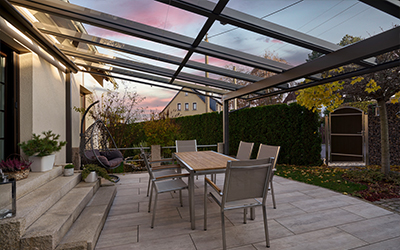 Überdachte Terrasse mit Glasdach, Sitzgruppe und Garten bei Abendstimmung