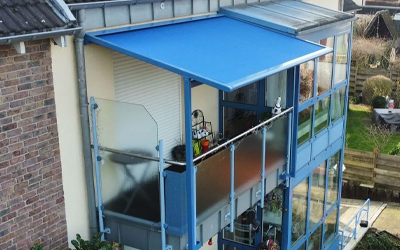 Balkon mit blauer Markise und Glas-Seitenelementen an einem Wohnhaus.