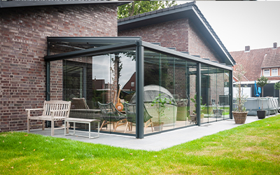 Moderner Sommergarten mit Glasfronten und dunkler Aluminiumkonstruktion an einem Backsteinhaus