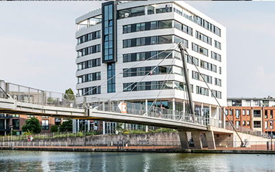 Modernes Bürogebäude am Wasser mit verglaster Fassade und Fußgängerbrücke