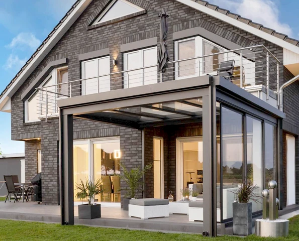 Moderne Terrassenüberdachung mit Glaswänden und Lounge-Bereich an einem Backsteinhaus