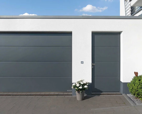Graues Garagentor mit passender Nebeneingangstür an einer modernen weißen Hausfassade