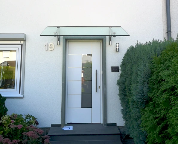 Moderne weiße Haustür mit Glaselement und Glasvordach an einem Wohnhaus