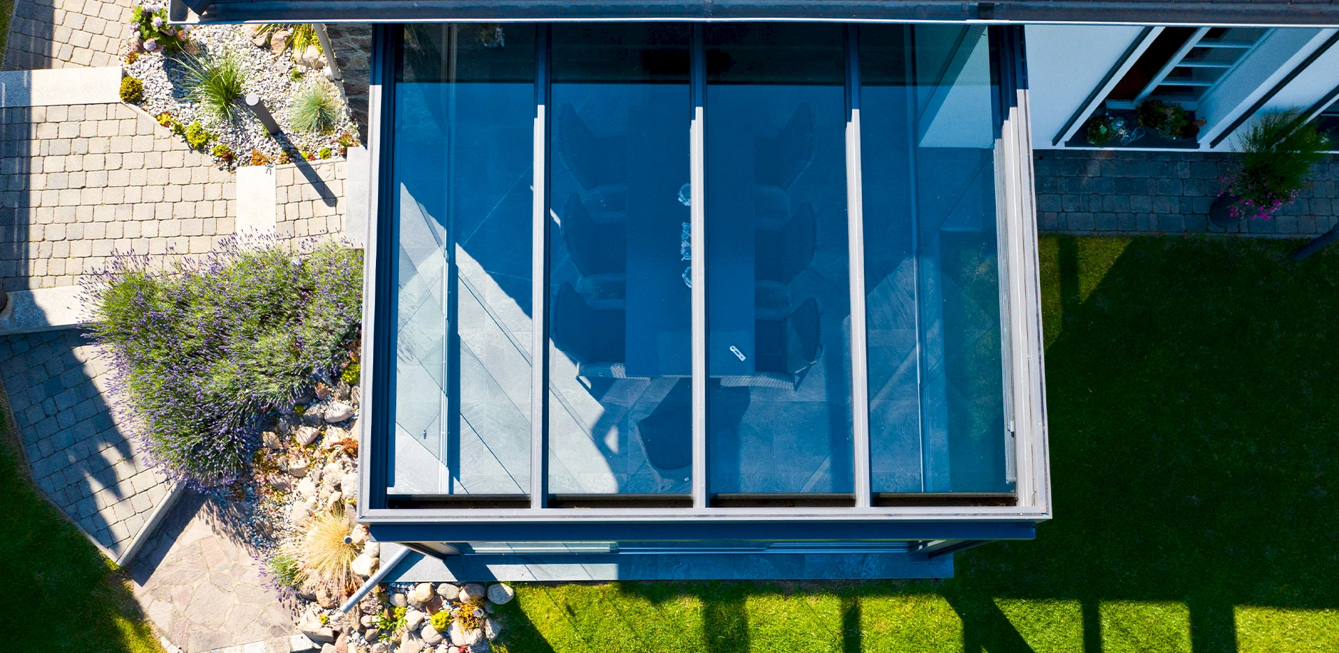 Sommergarten auf einer kleinen Terrasse mit rahmenlosen Glasschiebetüren, Essplatz und gemütlichem Sitzbereich.