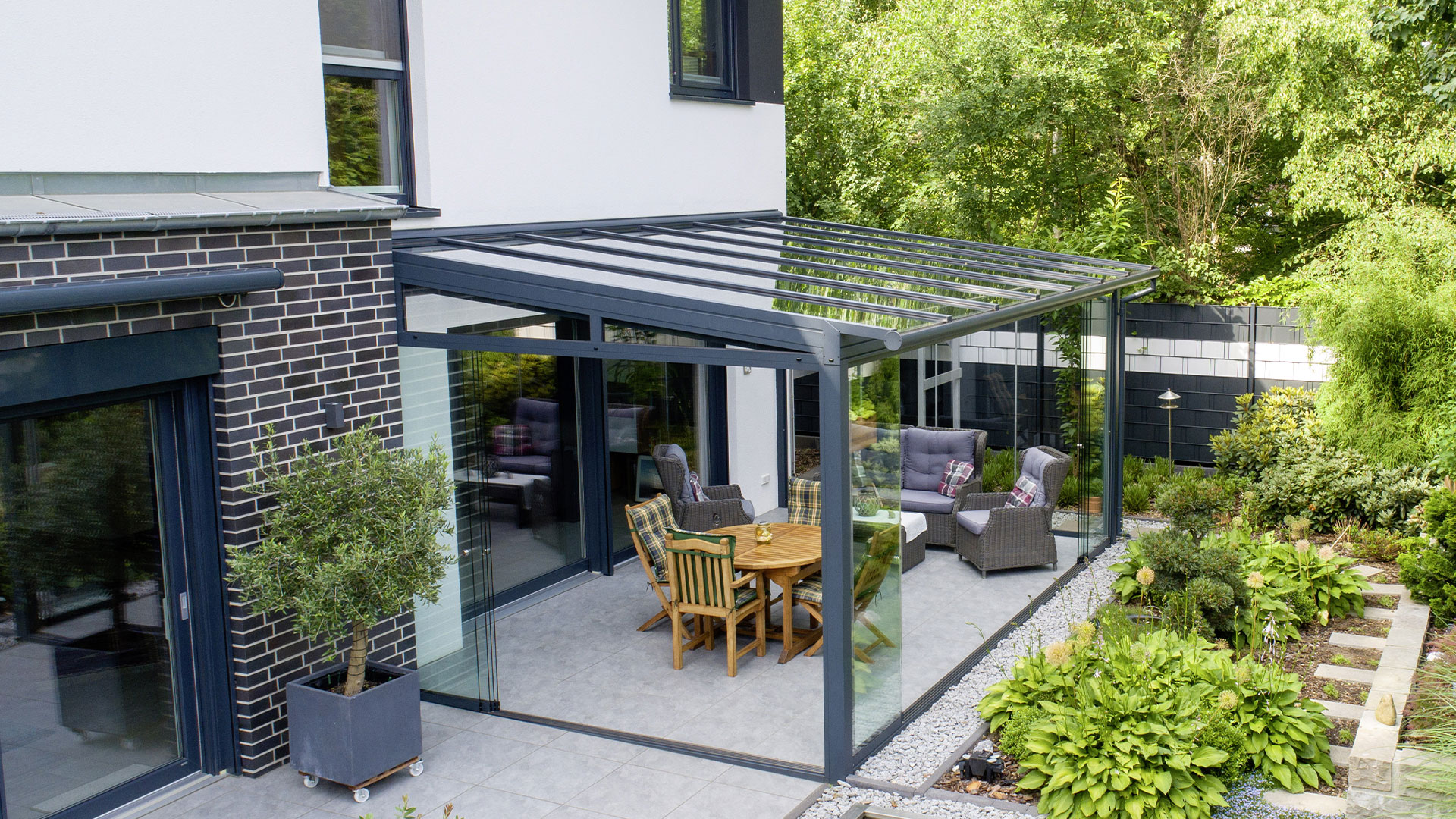 Sommergarten mit rahmenlosen Glasschiebetüren an einer Doppelhaushälfte mit Terrasse, Sitzbereich und begrüntem Garten