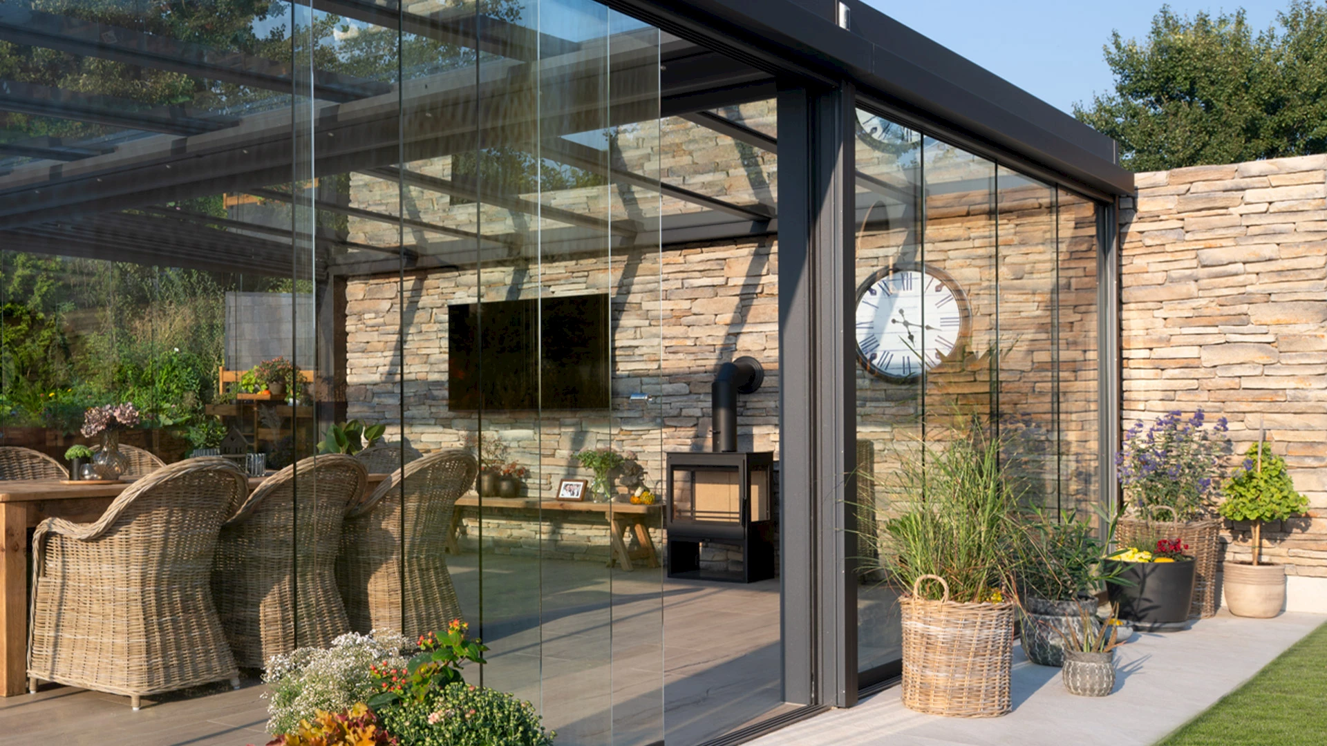 Moderner Sommergarten an einem Bungalow mit rahmenlosen Glasschiebetüren, Essplatz und direktem Übergang zum Garten